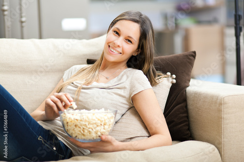 Photo: Beautiful young woman eating popcorn on the sofa Beautiful young woman eating popcorn on the sofa