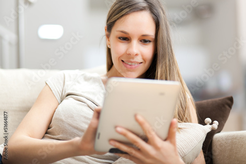 Photo: Young woman using a tablet on sofa at home Young woman using a tablet on sofa at home