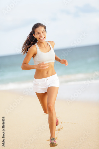 Photo: Runner woman running on beach smiling happy Runner woman running on beach smiling happy