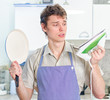 Young man wearing apron and holding pan and iron