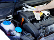 Close up of a hand with tools in front of an engine bay