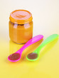 Baby food with weaning spoons on yellow background