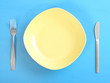 Photo: An empty ceramic plate with fork on a blue table. An empty ceramic plate with fork on a blue table.