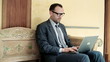 Businessman sitting on bench in antique hotel using laptop compu