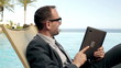 Young businessman chatting with tablet by swimming-pool in hotel