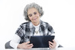 Oma sitzt am Tisch mit iPad in der Hand & guckt aufs Tablet