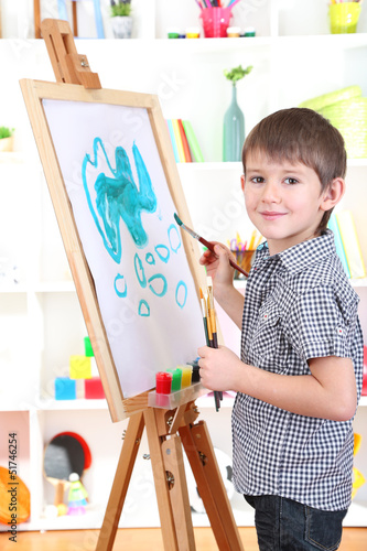 Photo: Little boy painting paints picture on easel Little boy painting paints picture on easel
