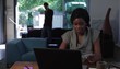 Black woman using credit card at home working on laptop with partner in background on phone  
