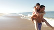 Man Giving Woman Piggyback As They Run Along Beach