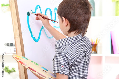 Photo: Little boy painting paints picture on easel Little boy painting paints picture on easel