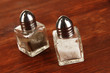 Containers for salt and pepper on wooden table close-up