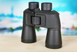 Black modern binoculars on wooden table on blue background