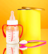 Bottle with milk and food for babies on orange background