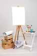 Wooden easel with clean paper and art supplies in room