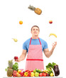 Man juggling with fruits behind a table full of fruits and veget