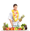 Man holding a pinneapple and posing behind a table with fruits a