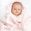 Foto: Caucasian baby boy covered with pink towel joyfully smiles at ca Caucasian baby boy covered with pink towel joyfully smiles at ca
