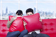 Couple hide behind pillow on red sofa