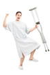 Happy male patient in hospital gown holding crutches and gesturi
