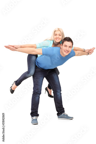 Photo: Full length portrait of a happy young couple posing piggyback Full length portrait of a happy young couple posing piggyback