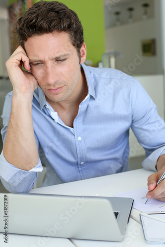 Photo: Man with doubtful look in front of laptop Man with doubtful look in front of laptop