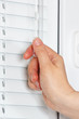 Hand closes the blinds on a white plastic window