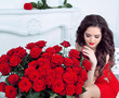 Beautiful young woman with red roses flowers bouquet in modern i