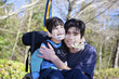 Photo: Little disabled boy in wheelchair hugging older brother outdoors Little disabled boy in wheelchair hugging older brother outdoors