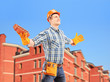 Happy worker holding a brick and spreading arms with a building