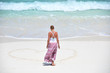 Girl drawing a heart on the sandy beach
