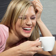 Junge hübsche Frau im Bett mit Kaffee lacht vor Freude