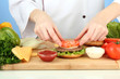 Photo: Female hands preparing cheeseburger, on blue background Female hands preparing cheeseburger, on blue background