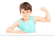 Foto: A mad child showing his muscles seated on a table A mad child showing his muscles seated on a table