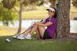 Happy female golfer relaxing under a tree on a sunny day
