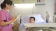 Female Doctor Talking To Boy In Hospital Bed