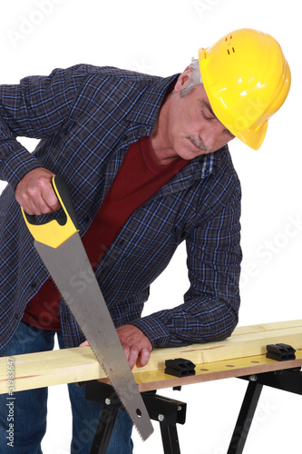 Photo: Construction worker sawing a plank of wood Construction worker sawing a plank of wood