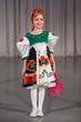 smiling little girl in folk costume with wrap performs on stage.