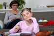 Photo: Little girl doing her homework whilst her mom is sewing Little girl doing her homework whilst her mom is sewing