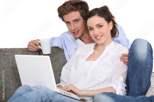 Photo: Couple using a laptop on a sofa Couple using a laptop on a sofa