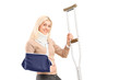 A happy blond female with broken arm holding a crutch