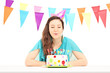 A smiling birthday female with a party hat blowing the candles o