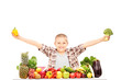 An excited kid holding broccoli, and a pepper on a table full of