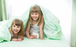 Two little girls lying under blanket on bed