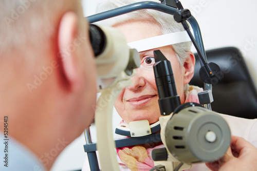 Photo: Senior woman behind slit lamp at optician Senior woman behind slit lamp at optician
