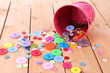 Colorful buttons strewn from bucket on wooden background