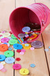Colorful buttons strewn from bucket on wooden background