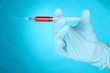 Hand holding syringe filled with blood on blue background