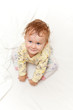 Photo: Joyful little girl sitting on bed and looking up at the camera Joyful little girl sitting on bed and looking up at the camera