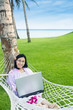 Asian student with laptop on hammock at beach