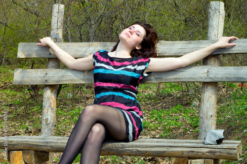 Photo: young dreamy girl sitting on a bench in the forest young dreamy girl sitting on a bench in the forest
